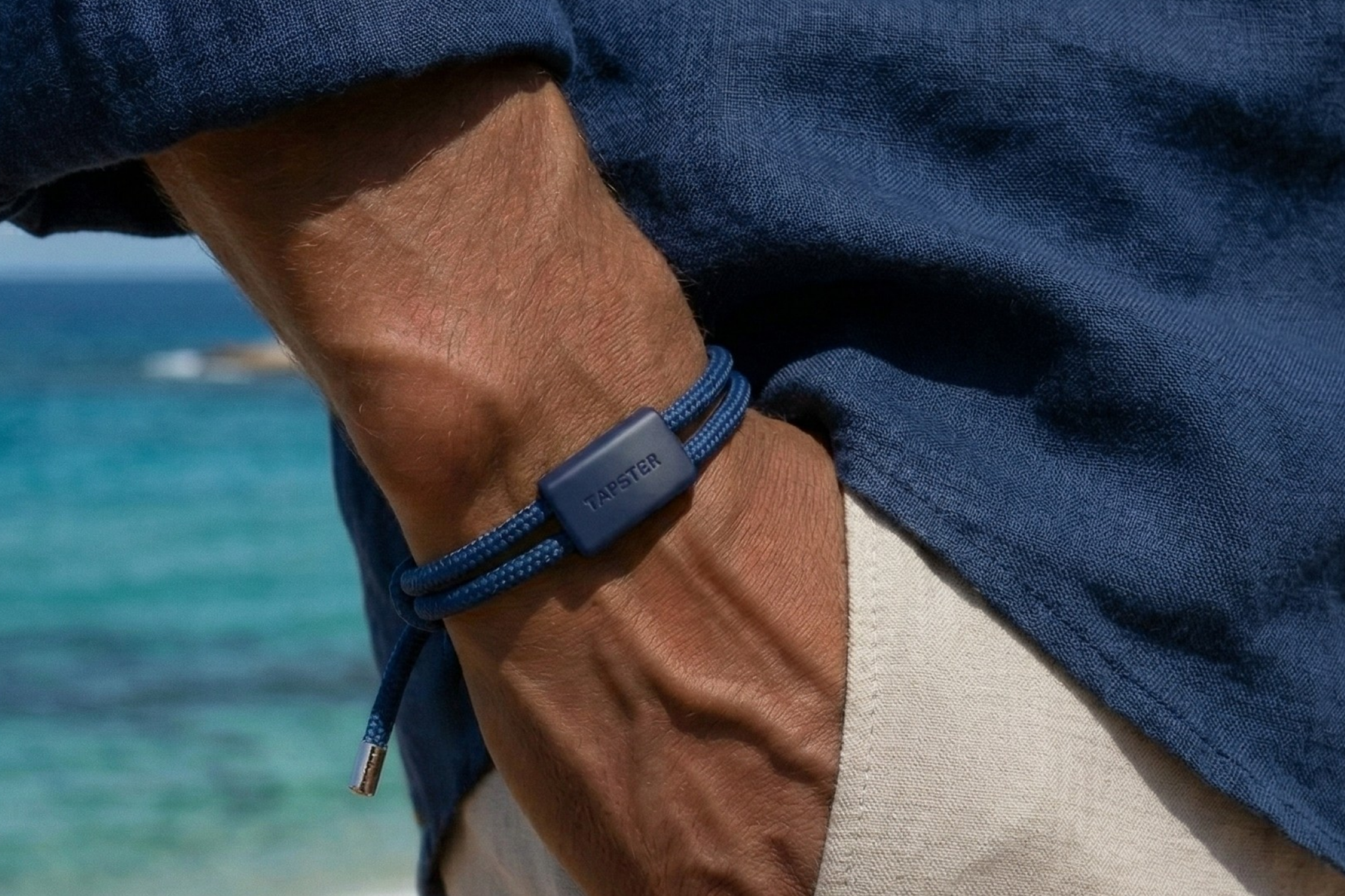 Person med blått Tapster-armbånd på håndleddet ved sjøen.