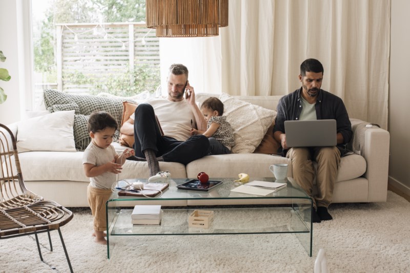 Par med to barn som sitter henslengt i sofa der en ser på PC og en er i mobilen.